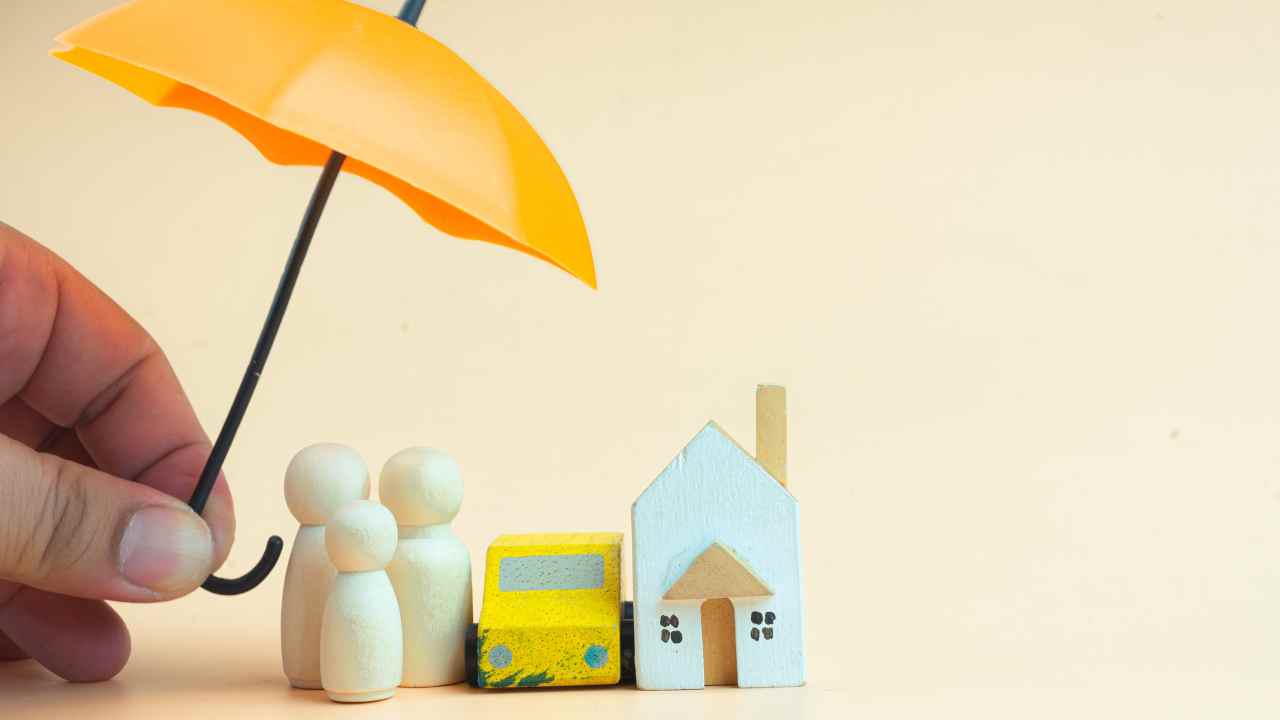 a small umbrella over figurines of a family card and home symbolizing coverage
